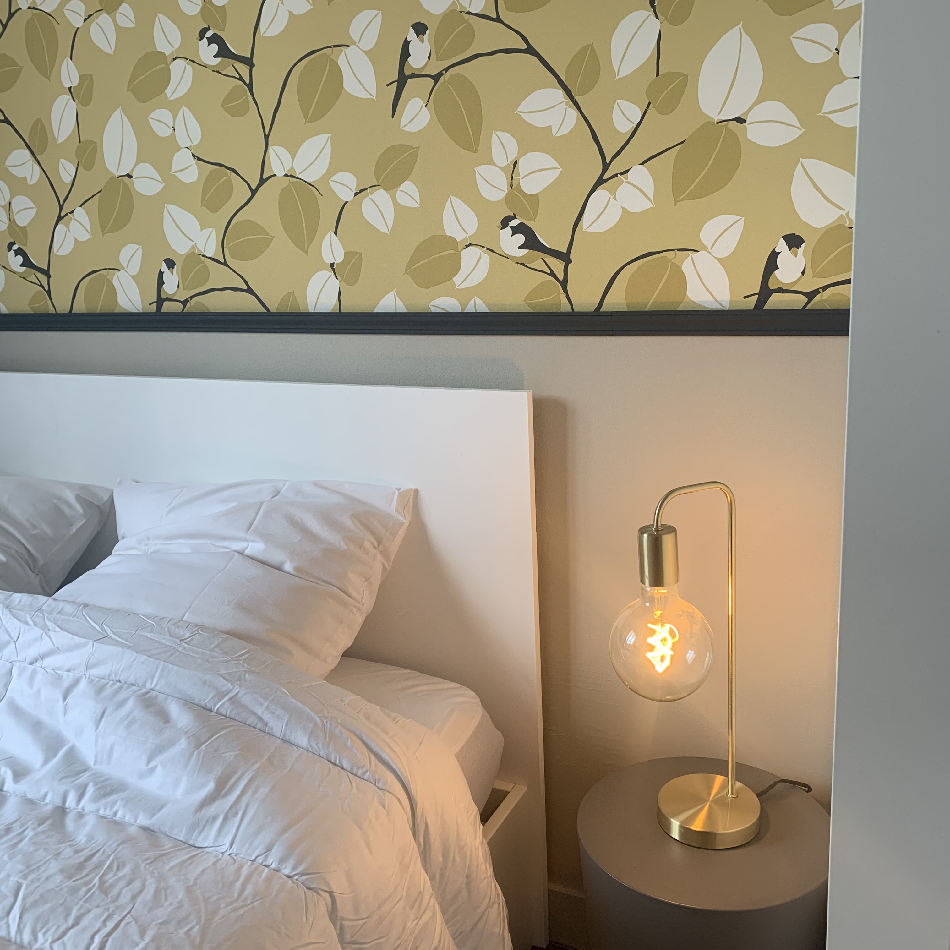 détails tête de lit blanche devant soubassement peinture papier peint oiseaux et baguette de finition avec chevet bubu et lampe en laiton