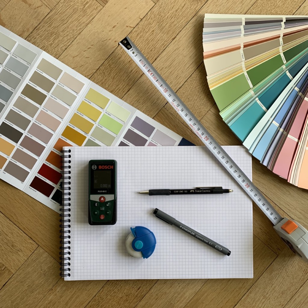 mise en scène bloc note, nuanciers de peinture, télémètre, mètre et crayons pour coaching déco et prise de cotes